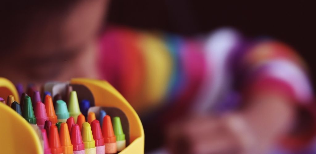 Fotografía de crayones de colores y de fondo una niña pintando