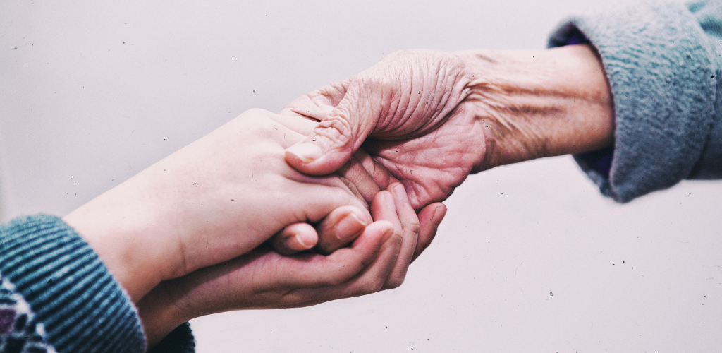 Foto de las manos de una persona joven sosteniendo la mano de una persona mayor.