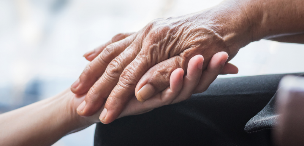 Foto de la mano de una persona mayor tomando la mano de una persona joven.