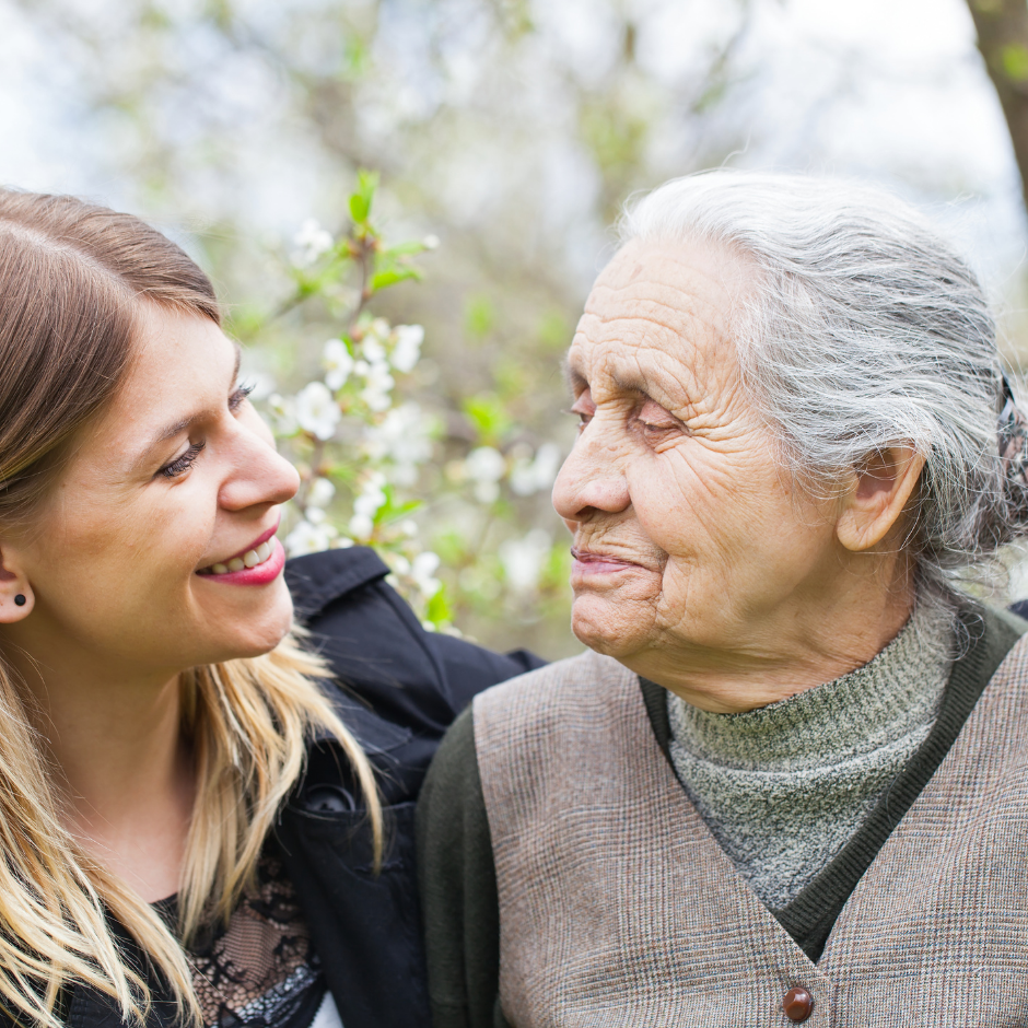 Foto de una mujer joven junto a una mujer mayor, en un jardín, abrazadas y sonriéndose