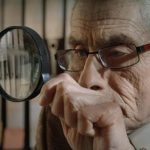 Foto de la película El Agente Topo donde se ve un hombre mayor mirando a través de una lupa.