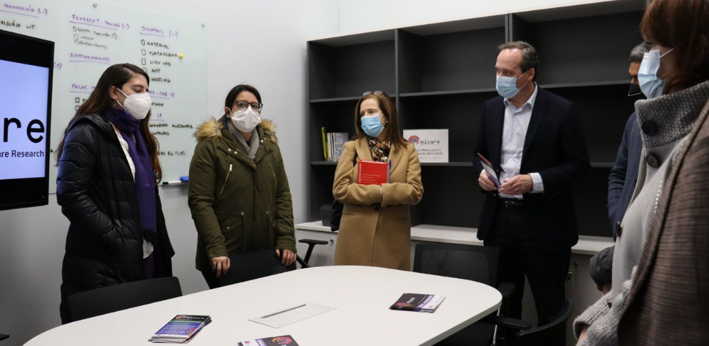 Foto de distintas personas de pie y usando mascarillas, al interior de una oficina, conversando entre ellas.