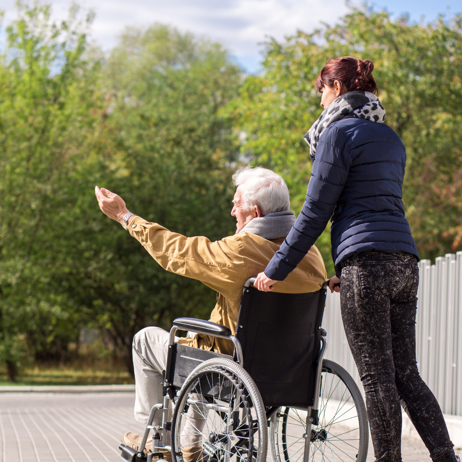 Foto de una mujer llevando a un hombre mayor en silla de ruedas.