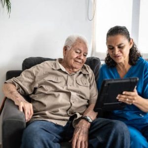 Home Caregiver showing tablet to senior man at his house