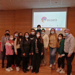Foto de un grupo de personas asistentes a la clase, dentro de una sala. Al fondo se ve una proyección con el logo de MICARE.