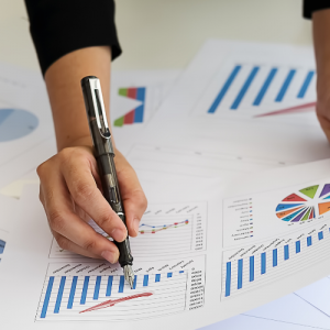 Foto de las manos de una mujer escribiendo sobre hojas con datos y gráficos