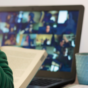 Fotografía de una persona conectada a una reunión de zoom y sosteniendo un libro.
