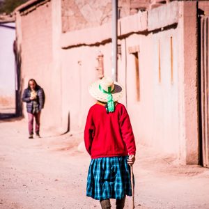 Foto de una mujer mayor de espaldas caminando por una calle de tierra en San Pedro de Atacama en Chile.