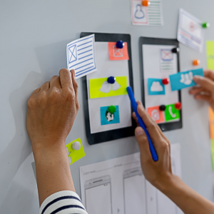 Foto de las manos de una persona diseñando una interfaz de un teléfono móvil sobre una pizarra con papeles adhesivos de colores