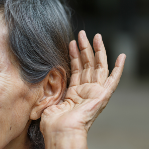 Una mujer mayor se pone la mano detrás de la oreja para tratar de escuchar mejor.