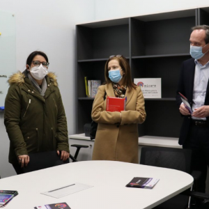 Foto de distintas personas de pie y usando mascarillas, al interior de una oficina, conversando entre ellas.