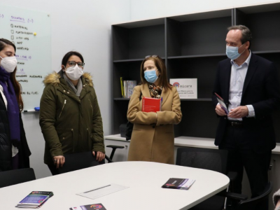 Foto de distintas personas de pie y usando mascarillas, al interior de una oficina, conversando entre ellas.