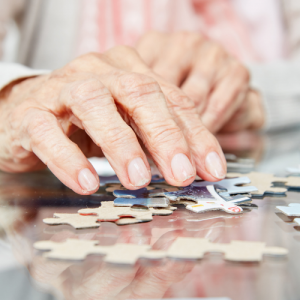 Foto de las manos de una mujer mayor armando un puzzle sobre una mesa