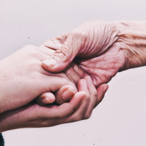 Foto de las manos de una persona joven sosteniendo la mano de una persona mayor.